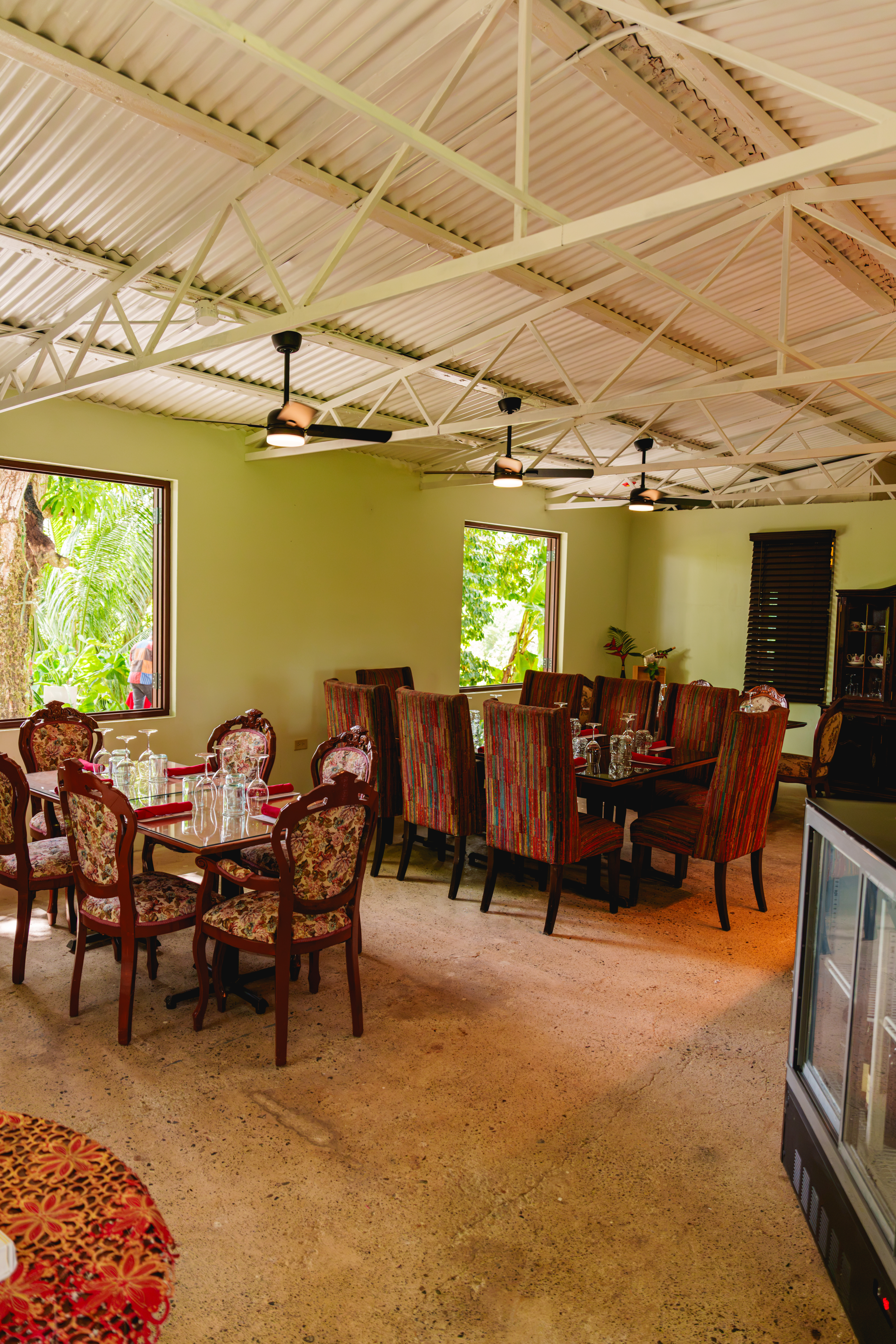 Comedor con paredes verde oliva, techo de zinc con vigas, dos mesas con sillas tapizadas y ventanas con vista a vegetación