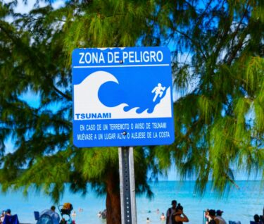 Bañistas frente a una señal de alerta de zona de tsunami escrita en español en una playa de Puerto Rico.